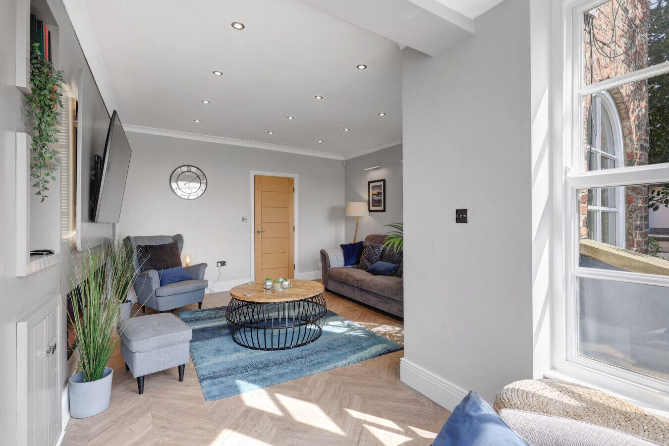 A modern living room with a round coffee table, two sofas, a wooden door, and a large window.