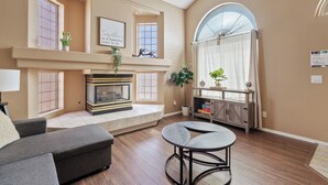 A living room with a fireplace, a sofa, a round table, and a large arched window. - Prime Glendale Location 8-Mins From Westgate Entertainment! (Glendale)