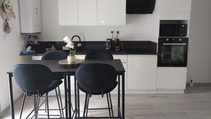 A modern kitchen with white cabinets, a black countertop, and a dining area with black chairs. - Spacious, bright studio with terrace in a quiet residence (Charly)