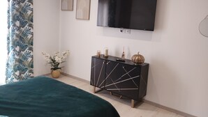A modern bedroom with a bed, a TV mounted on the wall, a black cabinet with geometric patterns, and a potted plant. - Spacious, bright studio with terrace in a quiet residence (Charly)