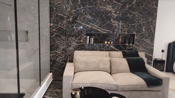 A modern living room with a black marble wall, a beige sofa, and a small black table. - Spacious, bright studio with terrace in a quiet residence (Charly)