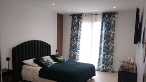 A modern bedroom with a large bed, a dark headboard, and tropical-themed curtains. - Spacious, bright studio with terrace in a quiet residence (Charly)