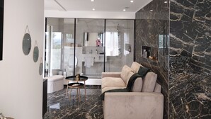 A modern living room with a sofa, a glass partition, and a view of a bathroom. - Spacious, bright studio with terrace in a quiet residence (Charly)
