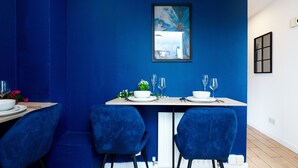 A dining area with a blue wall, a framed artwork, and a table set with white plates and blue chairs. - Open Mind Property - 1 Bed Flat with 3 Double Beds (Portsmouth)