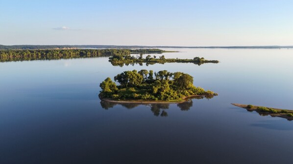 An aerial view of a small, lush island surrounded by calm water, with a distant shoreline visible.