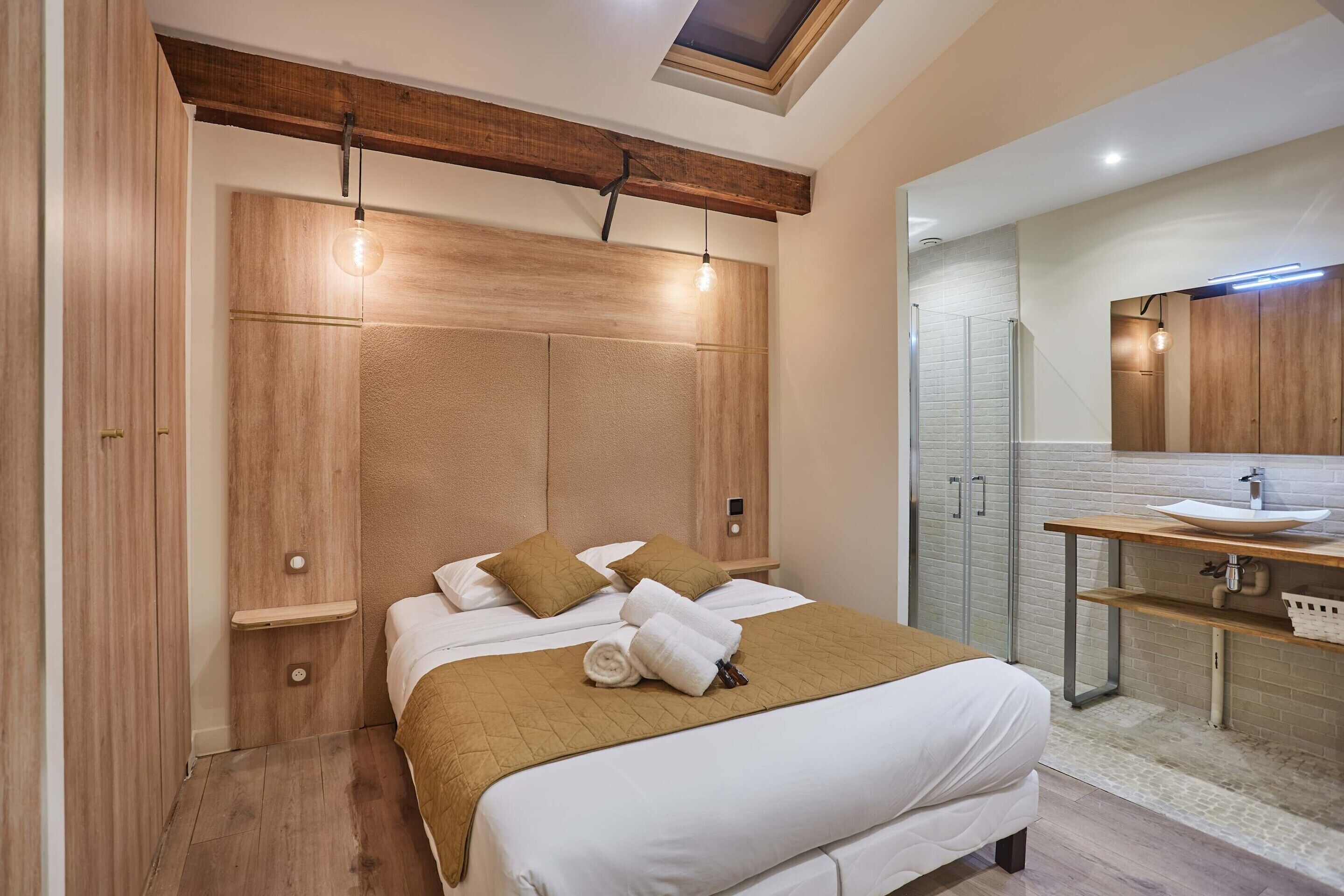 Une chambre moderne avec un grand lit, une tête de lit en bois et une coiffeuse intégrée avec un miroir.