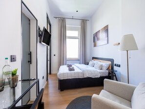 Habitación de hotel moderna con cama, televisor montado en la pared, escritorio con lámpara y vistas al exterior.