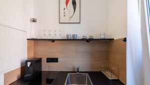 A modern kitchen with a black countertop, stainless steel sink, and a coffee machine. There is a wooden backsplash and a shelf with cups and glasses. - Apartment in Koblenz Near Deutsches Eck (Koblenz)
