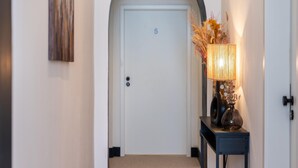 A hallway with a white door marked with the number 5, a small table with a lamp and dried plants, and a painting on the wall. - Apartment in Koblenz Near Deutsches Eck (Koblenz)
