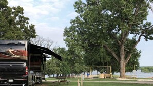 A recreational vehicle parked near a lakeside picnic area with tables and a swing set.