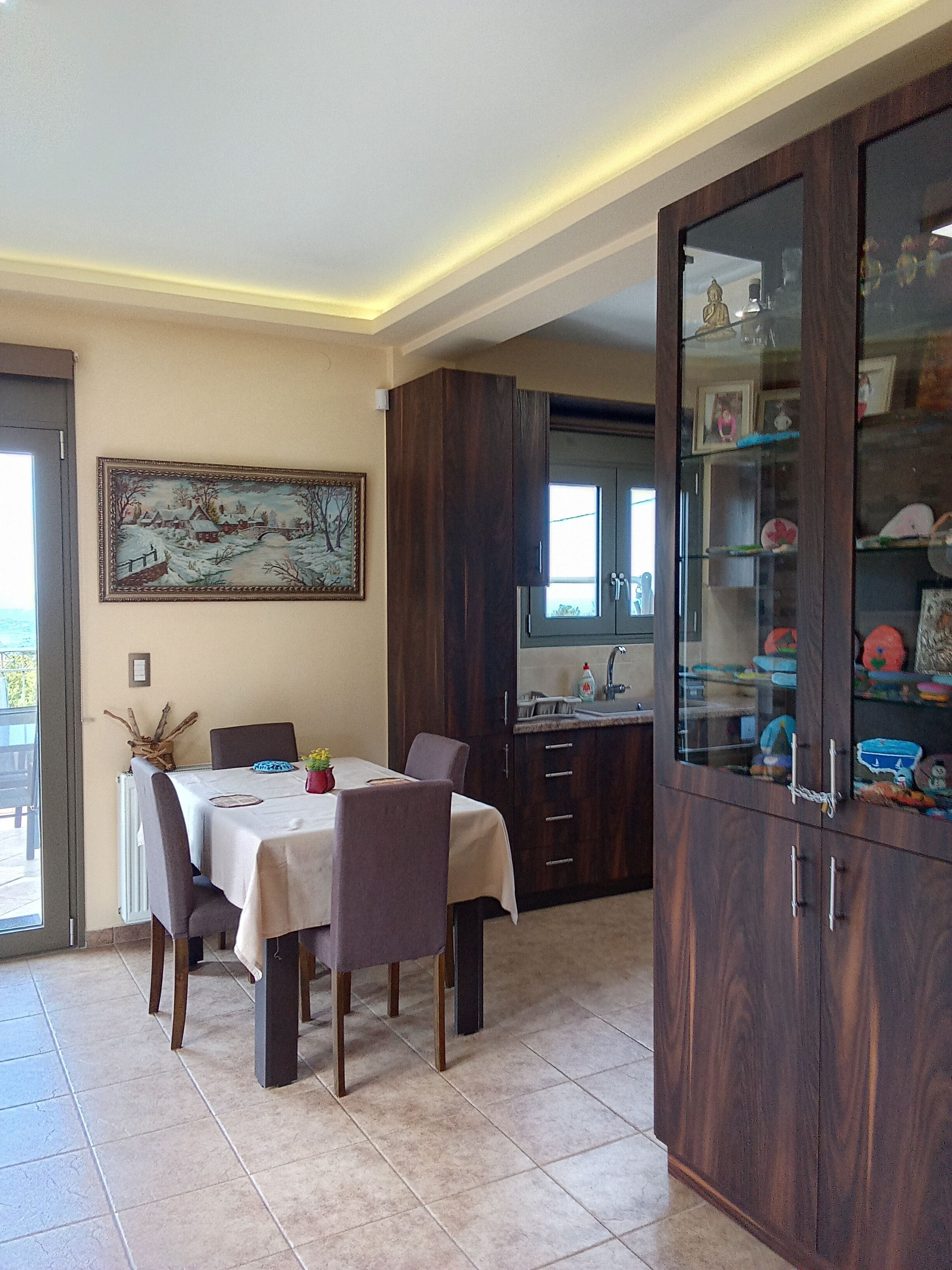 A dining area with a table set for four, a wooden cabinet with glass doors, and a painting on the wall.