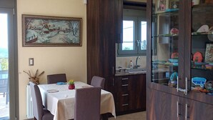 A dining area with a table set for four, a wooden cabinet with glass doors, and a painting on the wall. -  Villa Kastania – Cretan Nature Retreat (Melidoni Chania)