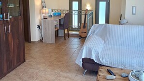 A bedroom with a bed, a desk, a chair, a guitar, and a wooden table with a bowl and stones. -  Villa Kastania – Cretan Nature Retreat (Melidoni Chania)