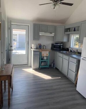 A kitchen with light grey cabinets, a teal cart, a microwave, and a ceiling fan.