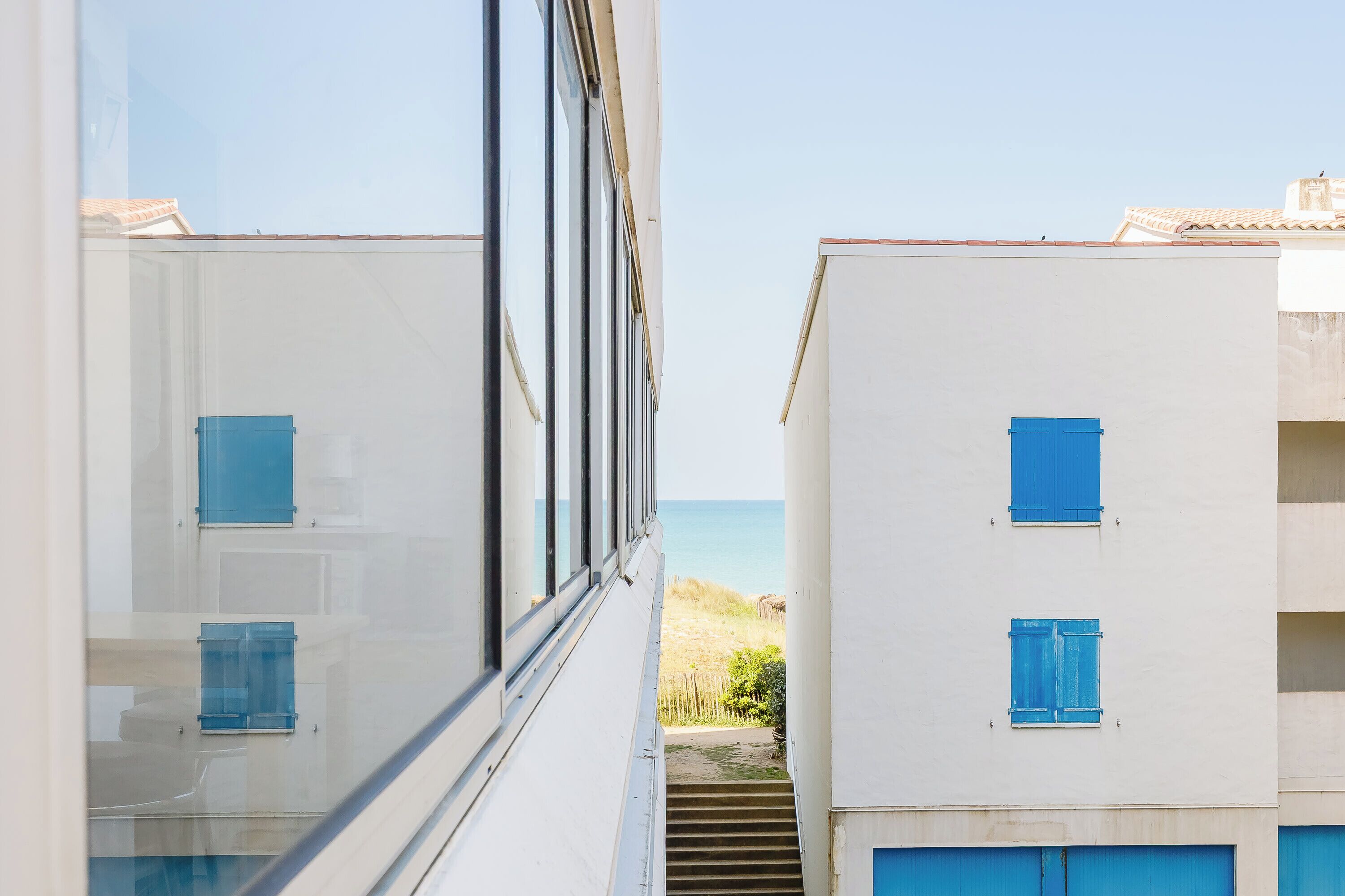 A narrow corridor with a view of the sea and a building with blue shutters.
