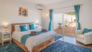 A bedroom with a large bed, a nightstand, a chair, and a view of the outdoor patio.