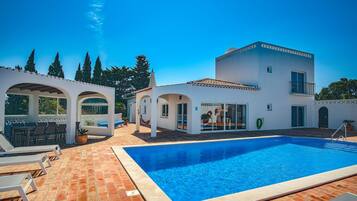 Una villa moderna con piscina, mobiliario exterior y un patio cubierto.