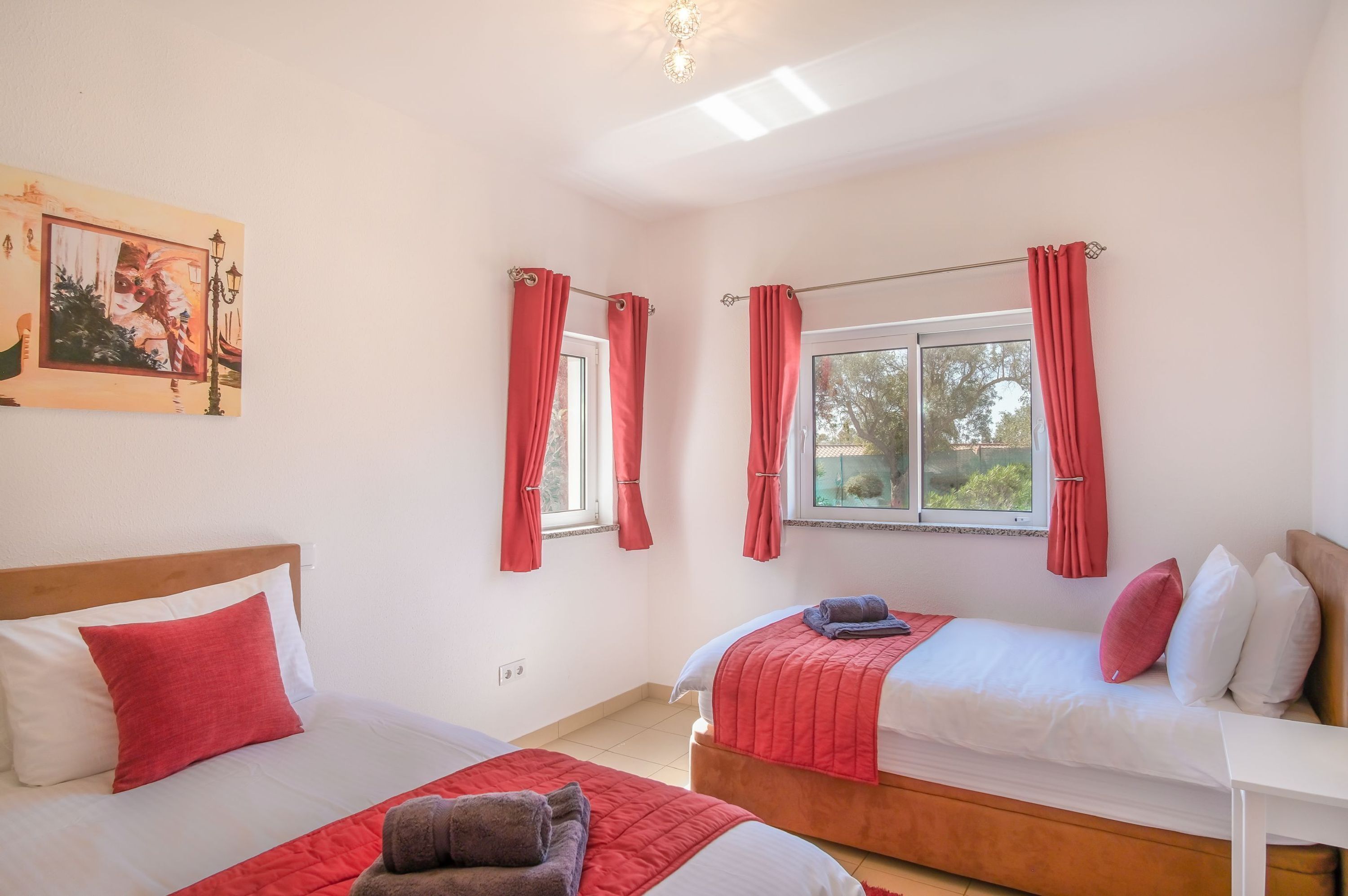 Una habitación con dos camas, cortinas rojas, un cuadro y una ventana con vistas.