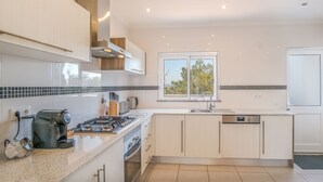 A modern kitchen with white cabinets, a stainless steel range, and a window with a view of trees.