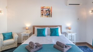A hotel room with a bed, two nightstands, a chair, and a wall-mounted air conditioner.