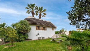 Une maison de plain-pied avec un toit de chaume, entourée d’une pelouse bien entretenue et de palmiers.