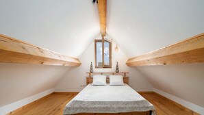 Une petite chambre mansardée, chaleureuse et accueillante, avec un lit en bois, une seule fenêtre et un plafond en pente.