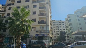 Un edificio de varios pisos con balcones, una palmera y coches estacionados.