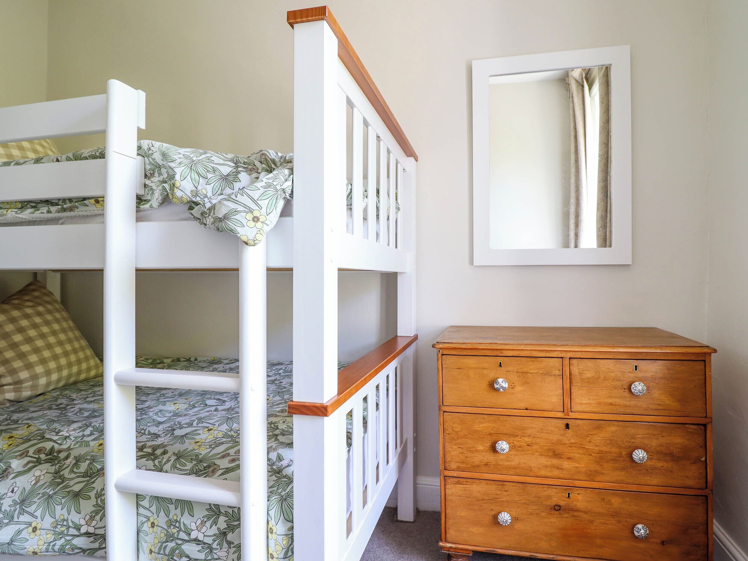 A bunk bed with floral bedding, a wooden dresser with drawers, and a mirror on the wall.