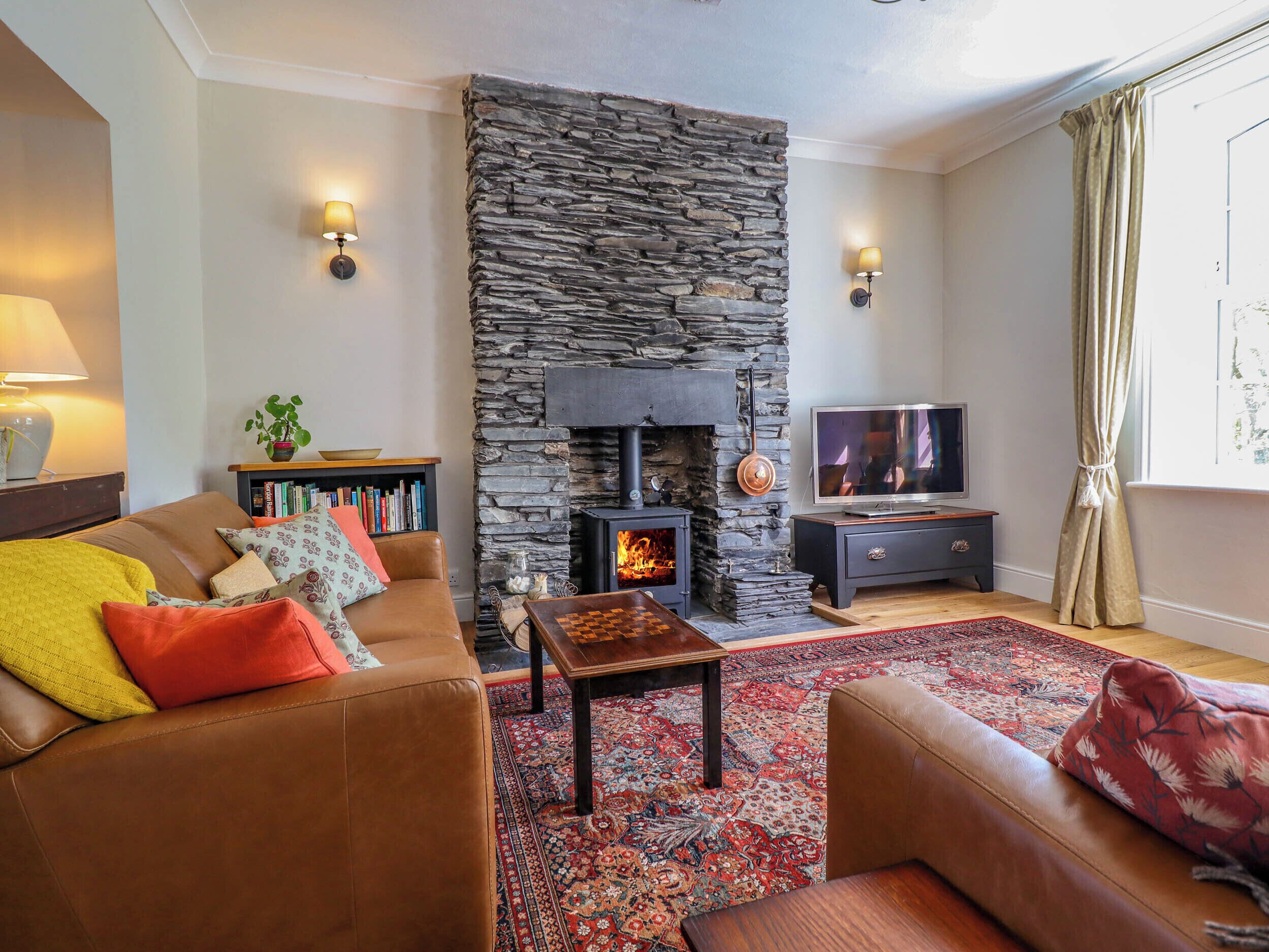 Una sala de estar acogedora con chimenea de piedra, sofás de cuero, un televisor y una estantería.