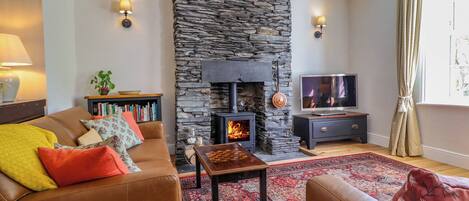 A cozy living room with a stone fireplace, leather sofas, a TV, and a bookshelf.
