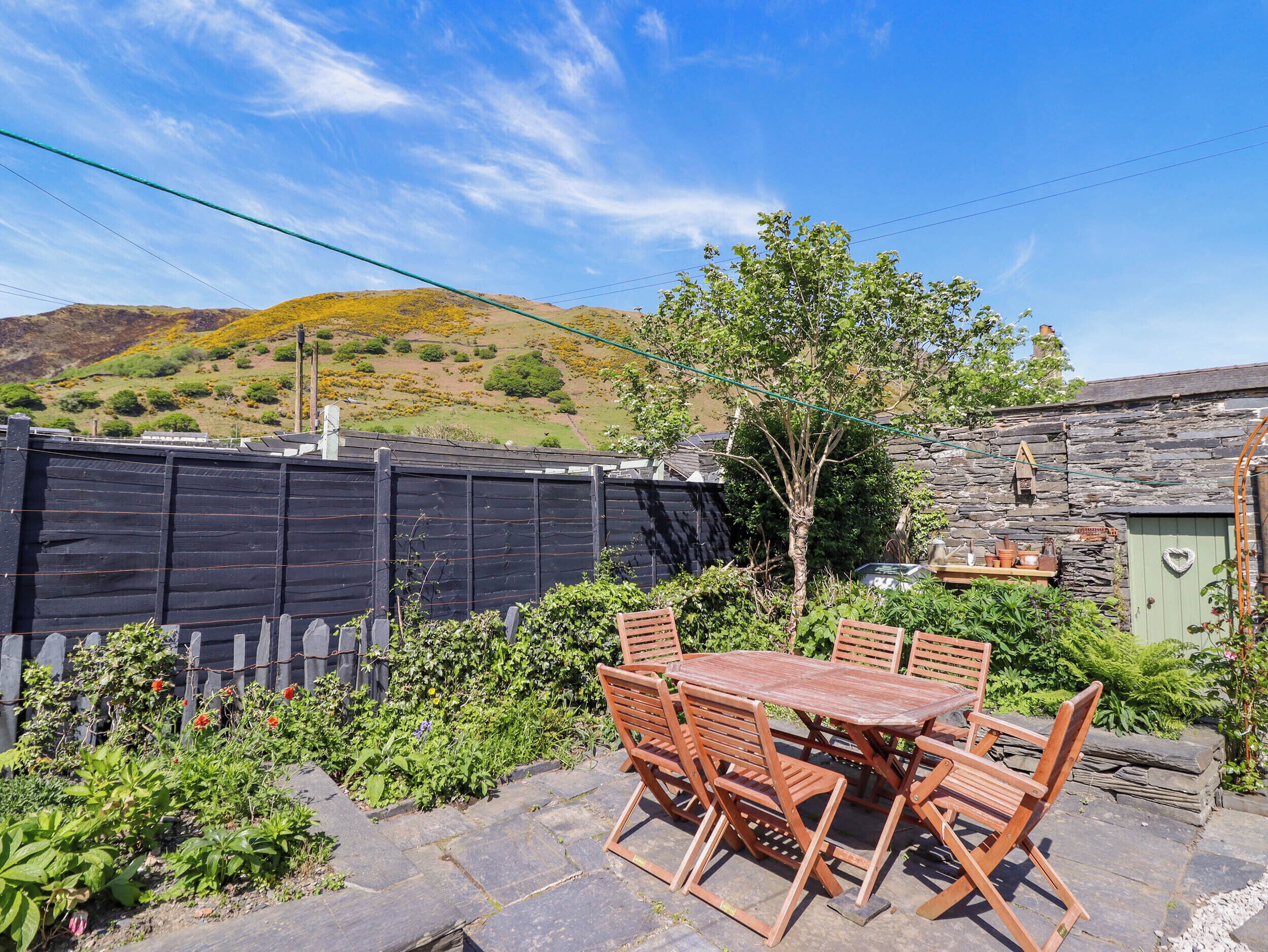 A patio with a wooden table and chairs, surrounded by a stone wall and a wooden fence.