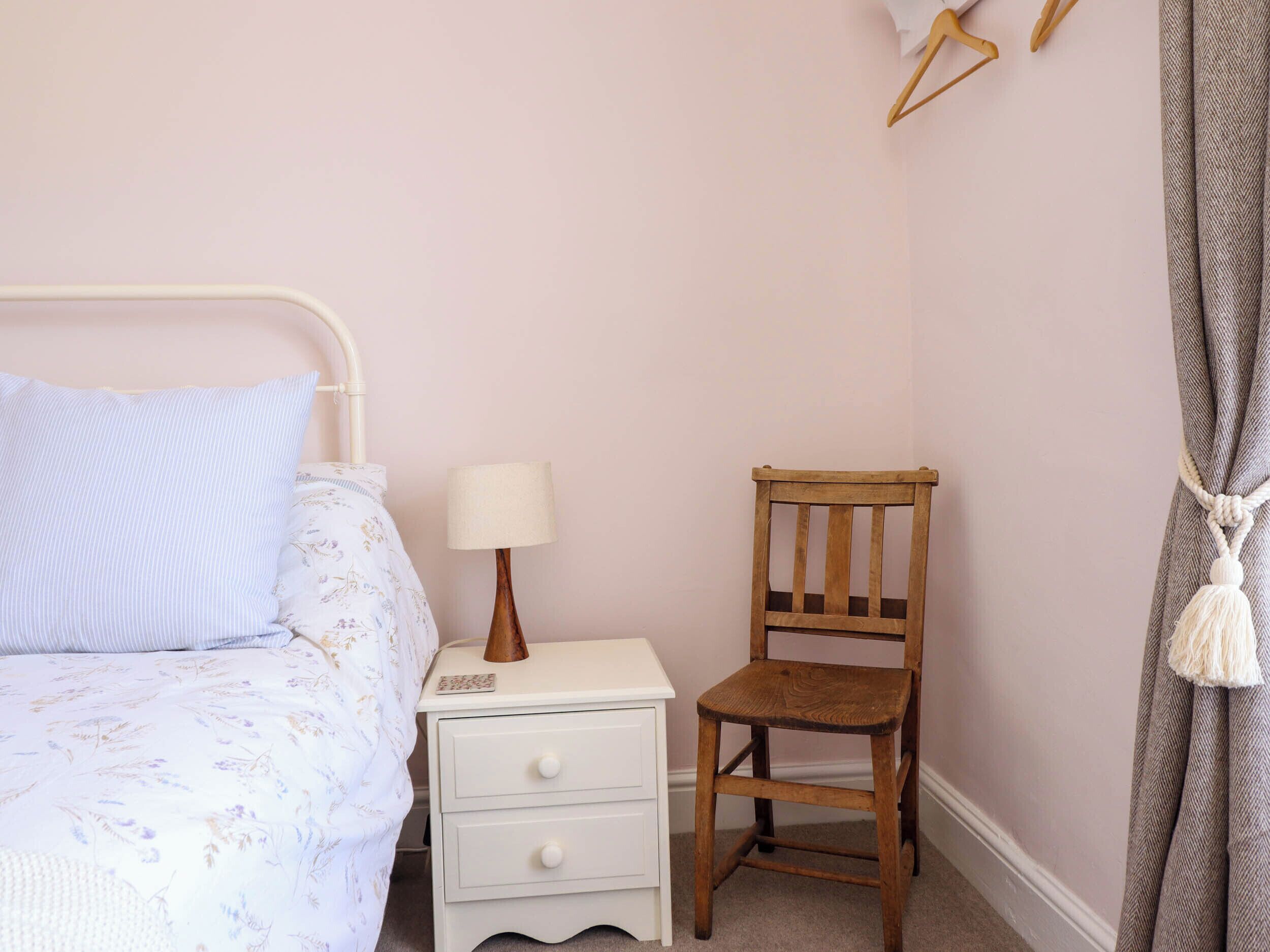 A bedroom with a bed, a nightstand, a wooden chair, a lamp, and a curtain.