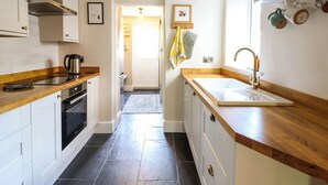 Une cuisine moderne avec des meubles blancs, un plan de travail en bois, un four encastré et un évier doté d’un robinet en laiton.