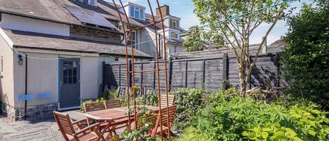 Un patio con mesa y sillas de madera, rodeado de abundante vegetación y una valla de madera.