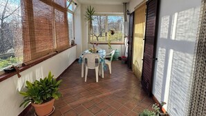 A sunlit patio with a tiled floor, a table with chairs, potted plants, and a view of the outdoors. - Detached cottage among the pines of Sila (CS) (Rose)