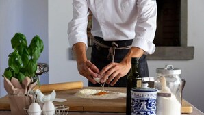 Een kok bereidt eten met ingrediënten en keukengerei op een houten tafel.
