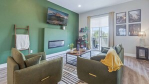 Ein Wohnzimmer mit grünen Wänden, einem Kamin, einem Fernseher und einem großen Fenster mit Vorhängen.