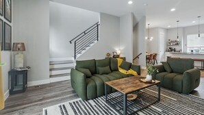 Ein modernes Wohnzimmer mit einem grünen Sofa, einem Holztisch und einer Treppe, die in einen Küchenbereich führt.