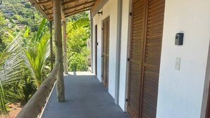 A covered corridor with wooden doors and a view of lush greenery. - Suítes Yvi Porã (Ilhabela)