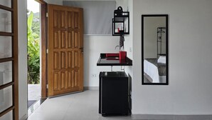 A hotel room with a wooden door, a black suitcase, a red sink, a mirror, and a bed. - Suítes Yvi Porã (Ilhabela)