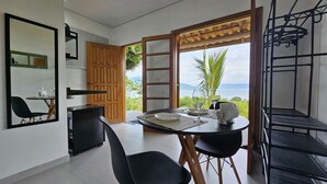 A dining area with a table set for two, a wooden door, a mirror, and a view of the outdoors. - Suítes Yvi Porã (Ilhabela)