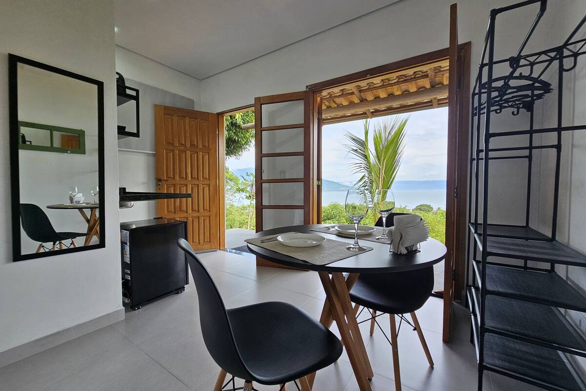 A dining area with a table set for two, a wooden door, a mirror, and a view of the outdoors.