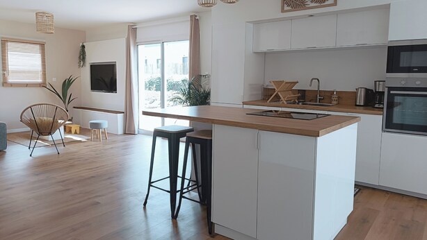Een moderne keuken met witte kasten, een houten aanrecht en een inbouwoven. Er zijn barkrukken en een hanglamp.