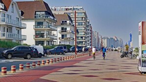 Eine Küstenpromenade mit modernen Gebäuden, einem Fahrradweg und parkenden Autos.