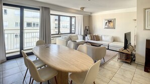 Ein modernes Wohnzimmer mit Essbereich, großen Fenstern und einem Balkon.
