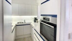 Eine kompakte Küche mit weißen Schränken, einem Edelstahlspülbecken, einer Kaffeemaschine und einem eingebauten Backofen.