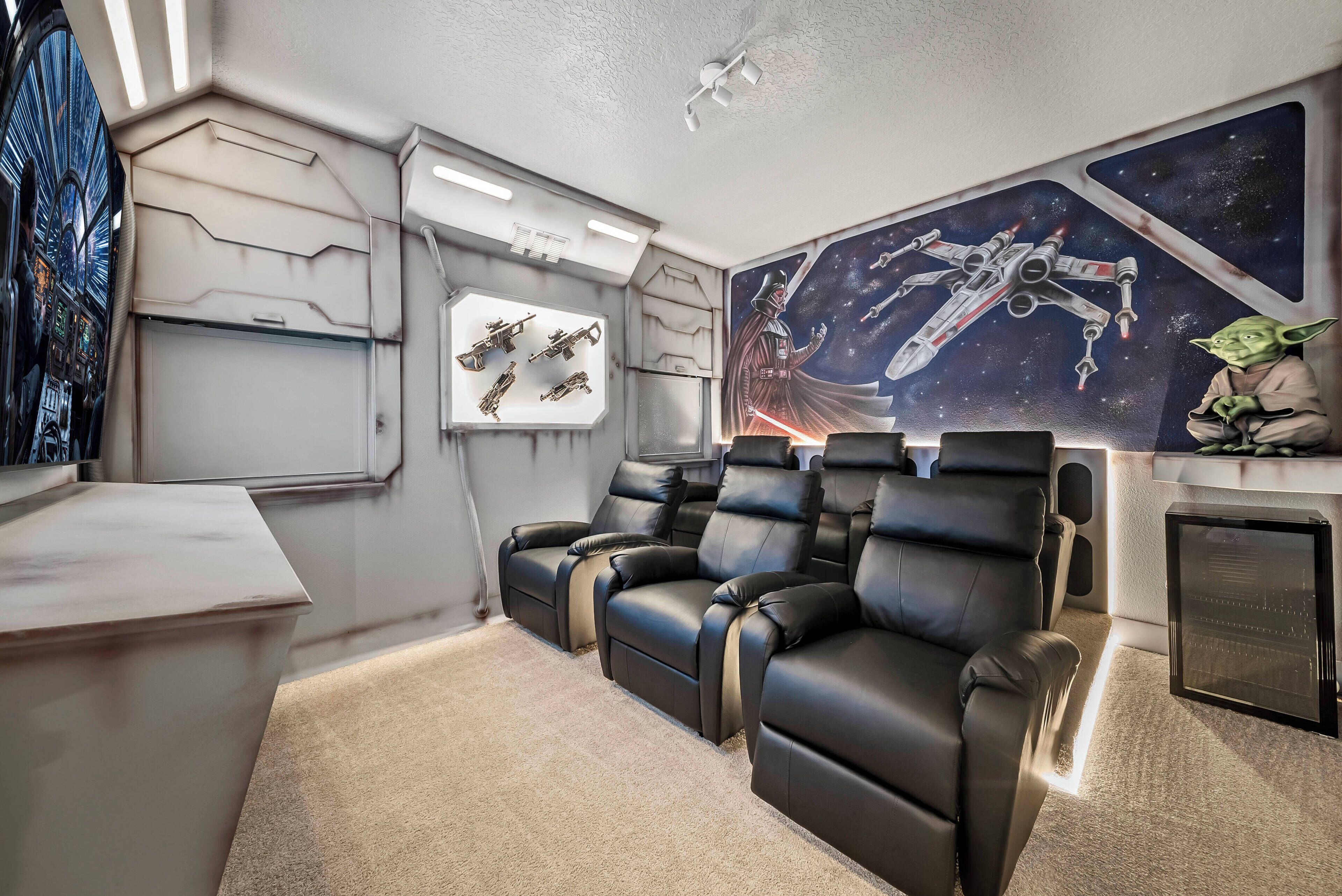 A room with a reclining chair set, a wall-mounted TV, and a Star Wars-themed mural.