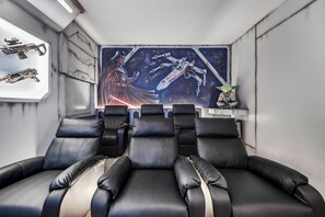 Una habitación con sillones de cuero negro reclinables, un mural con temática de Star Wars y una pequeña figura de Yoda.