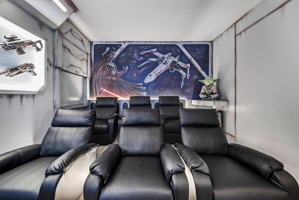 A room with reclining black leather chairs, a Star Wars-themed mural, and a small Yoda figurine.