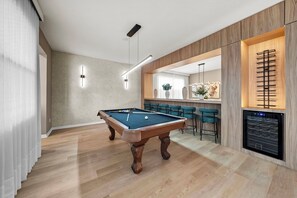Una mesa de billar en una habitación moderna con suelo de madera, una zona de bar y un horno empotrado.